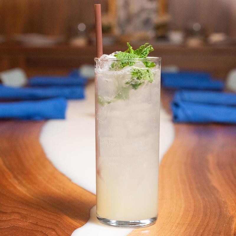 Tall glass of iced mojito with mint leaves and a straw on a wooden table with blue napkins.