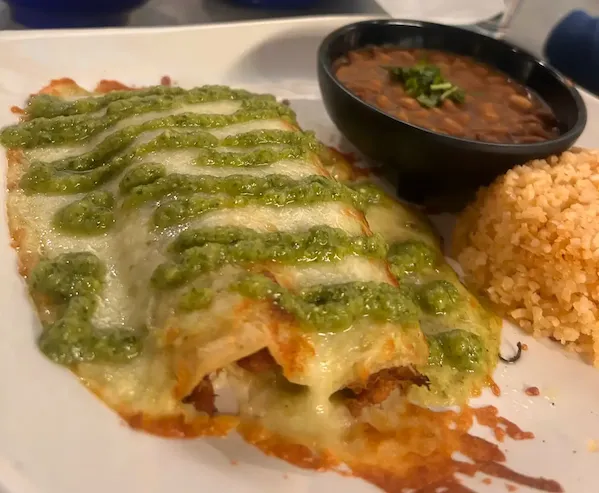 Plate with enchiladas topped with green sauce, served with refried beans and Mexican rice.