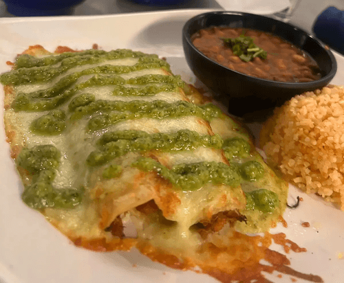 Plate with enchiladas topped with green sauce, served with refried beans and Mexican rice.