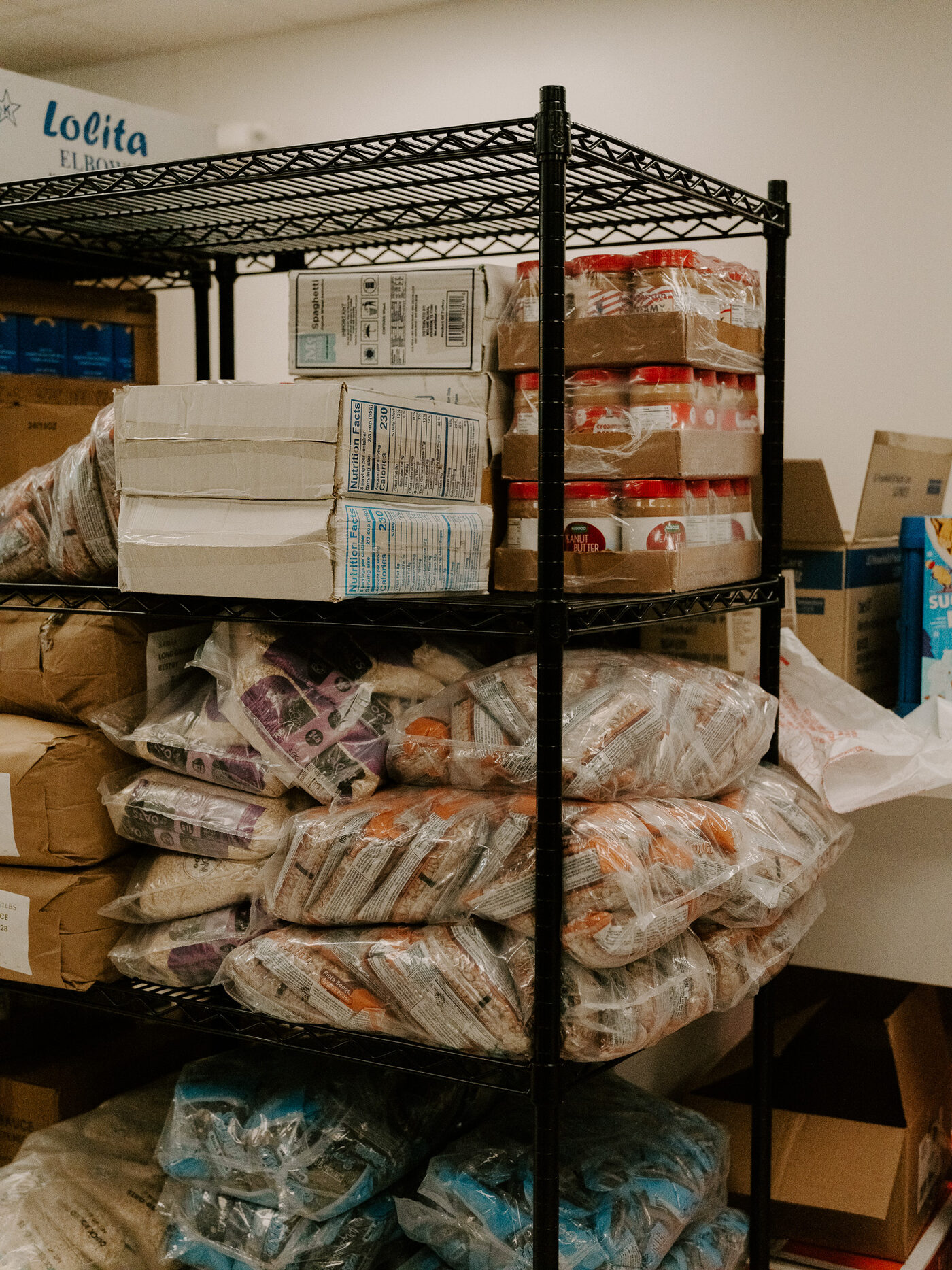 Stocked shelving at the Oak Cliff Veggie Project distribution site, holding frozen goods and dry pantry boxes
