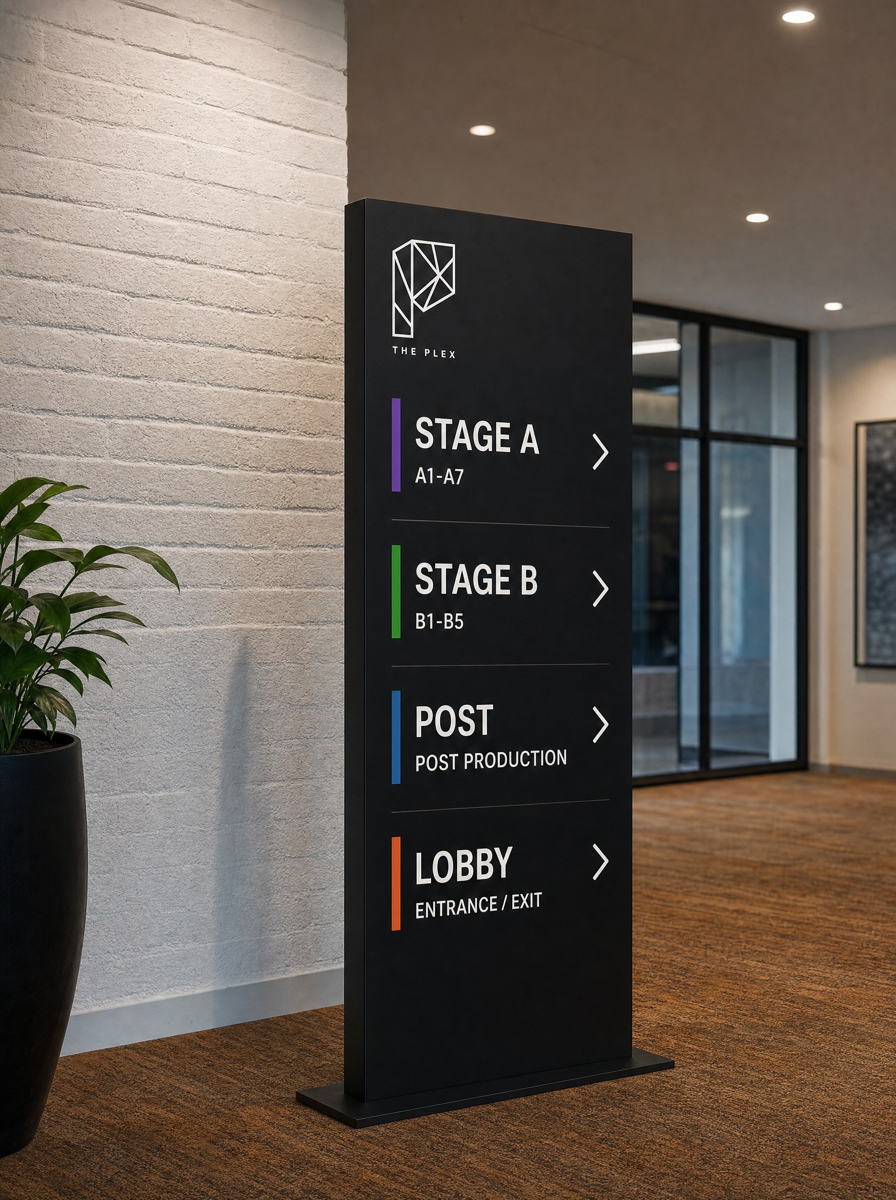 Lobby directory totem at The Plex listing Stage A, Stage B, Post and Lobby, each keyed to a signal colour, wayfinding by Good Word Agency