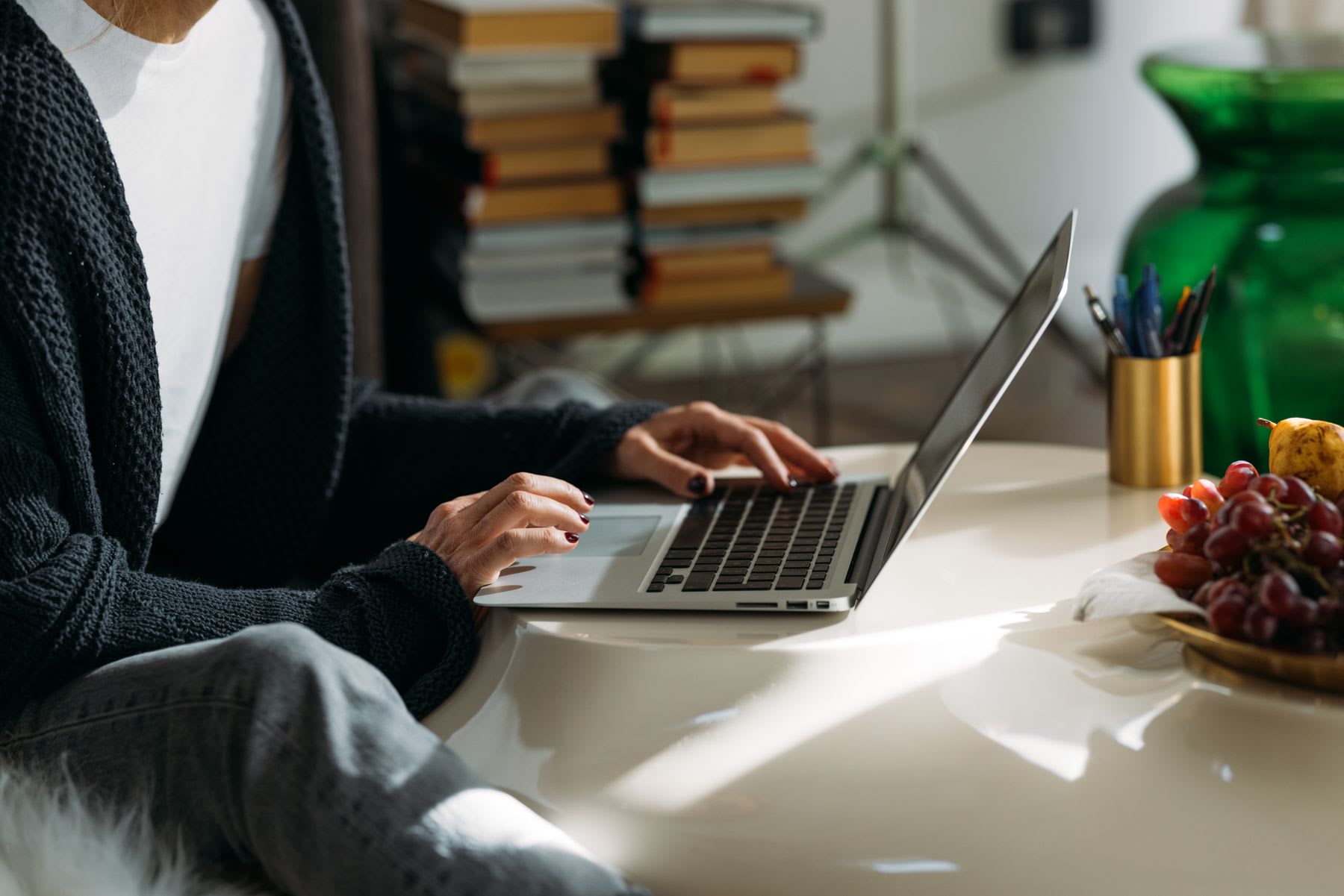 A woman working at a laptop on a kitchen table, shot over the shoulder in daylight