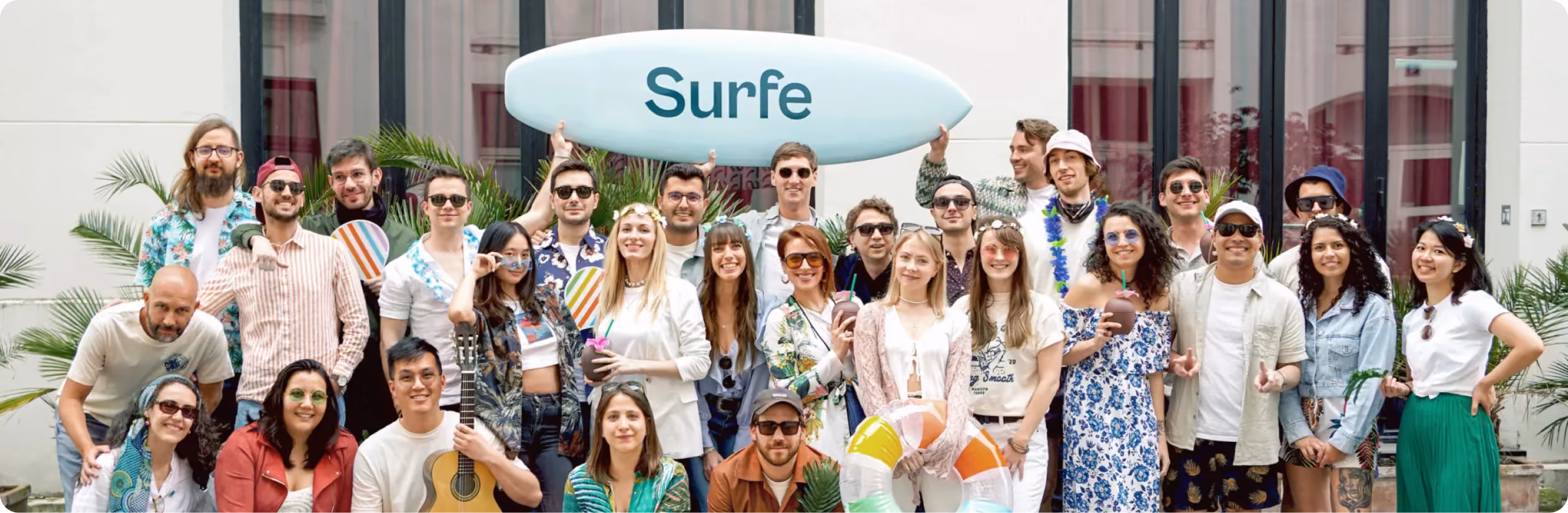 Large group photo of the Surfe team posing outdoors together holding a surfboard branded with the Surfe logo.
