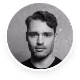 Black-and-white circular headshot portrait of a man with short hair and stubble.