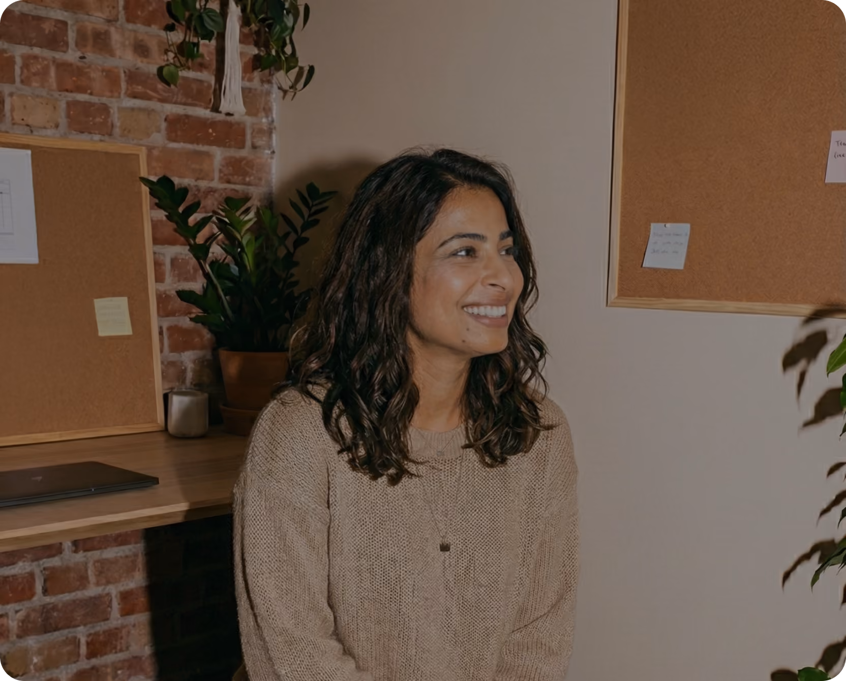Photo of a smiling sales development rep standing in an office with a brick wall and plants
