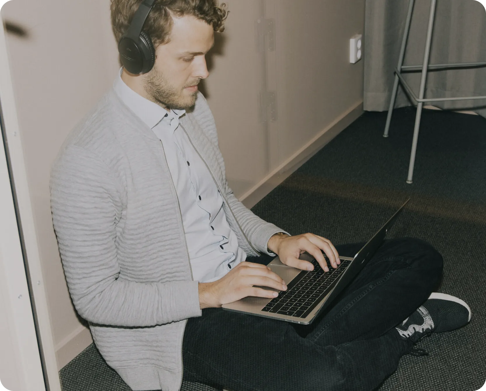 Man wearing headphones sits cross-legged on the floor typing on a laptop.
