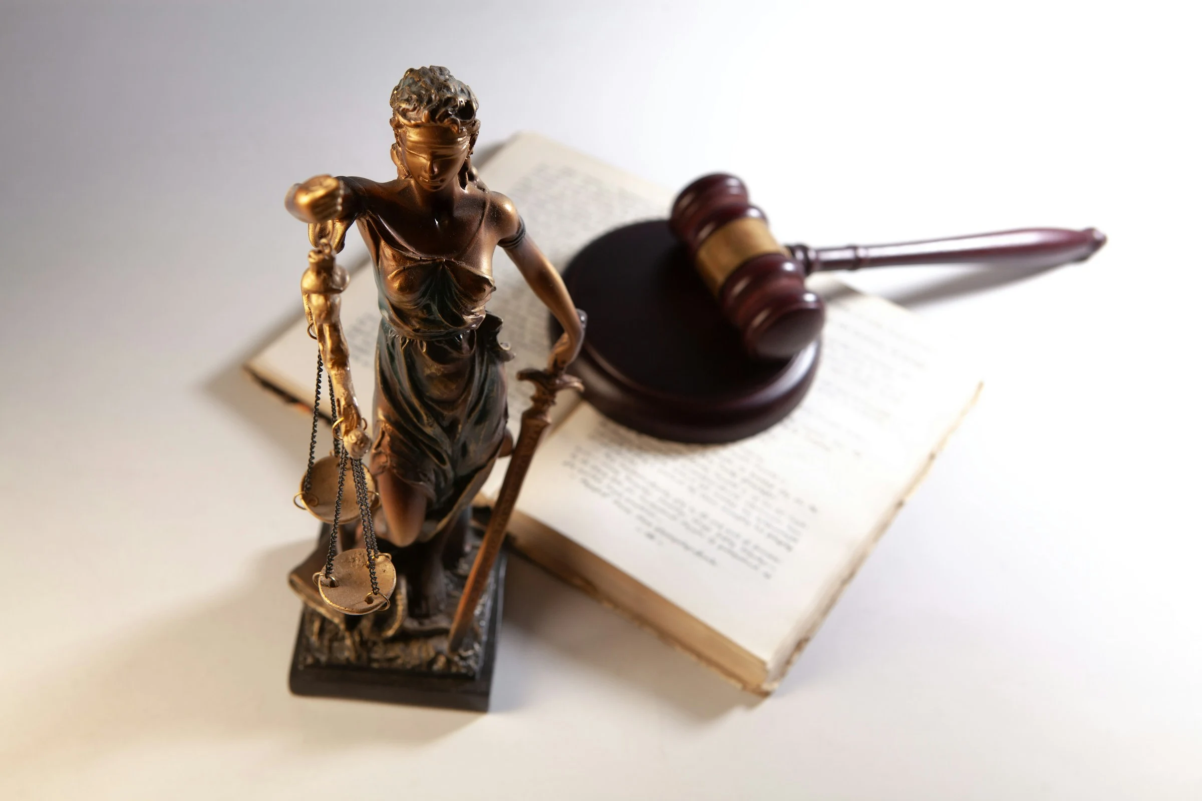 Blindfolded Lady Justice statue with scales and sword next to a gavel resting on an open book.