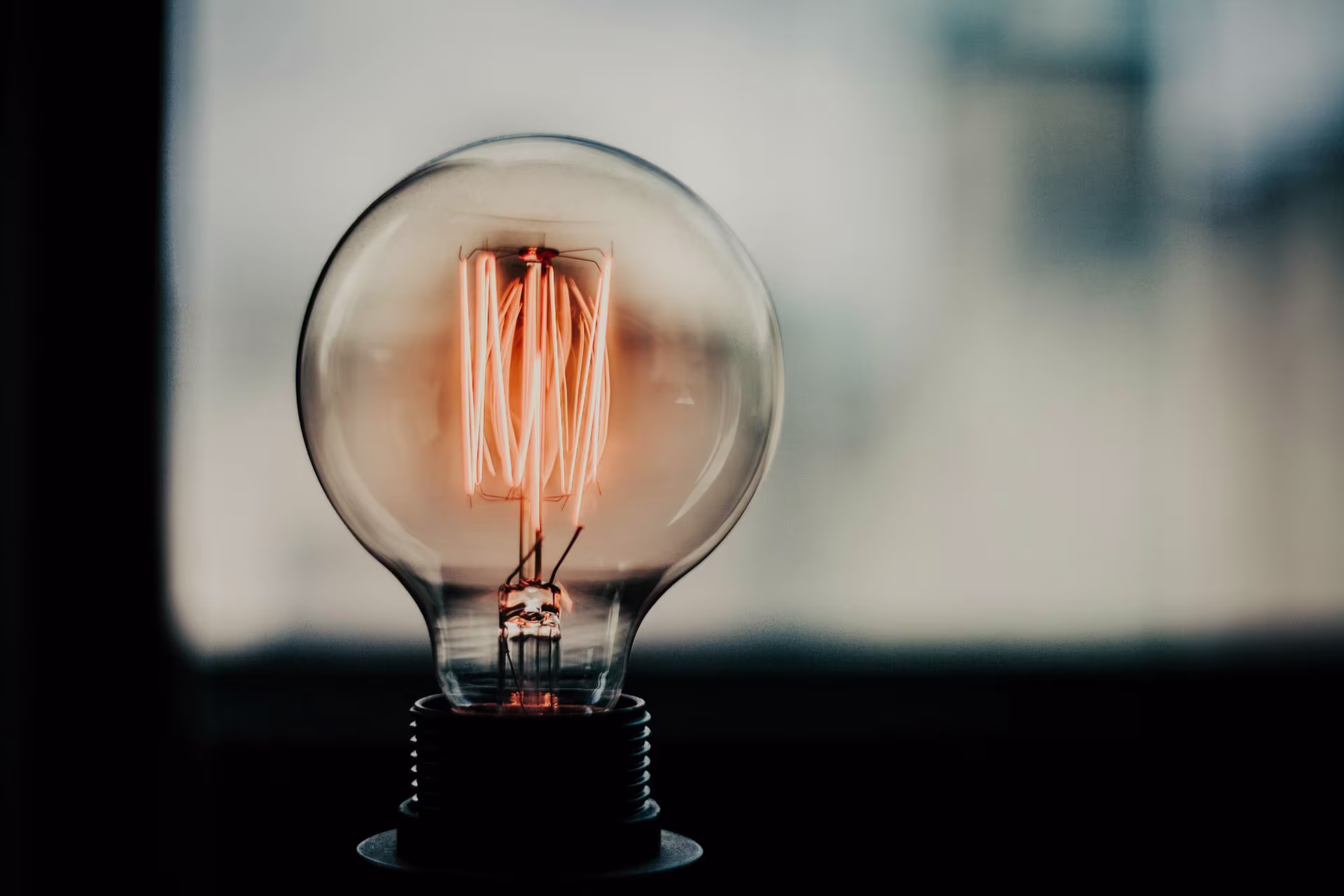 Close-up of a glowing vintage light bulb filament inside a glass bulb with a blurred background.