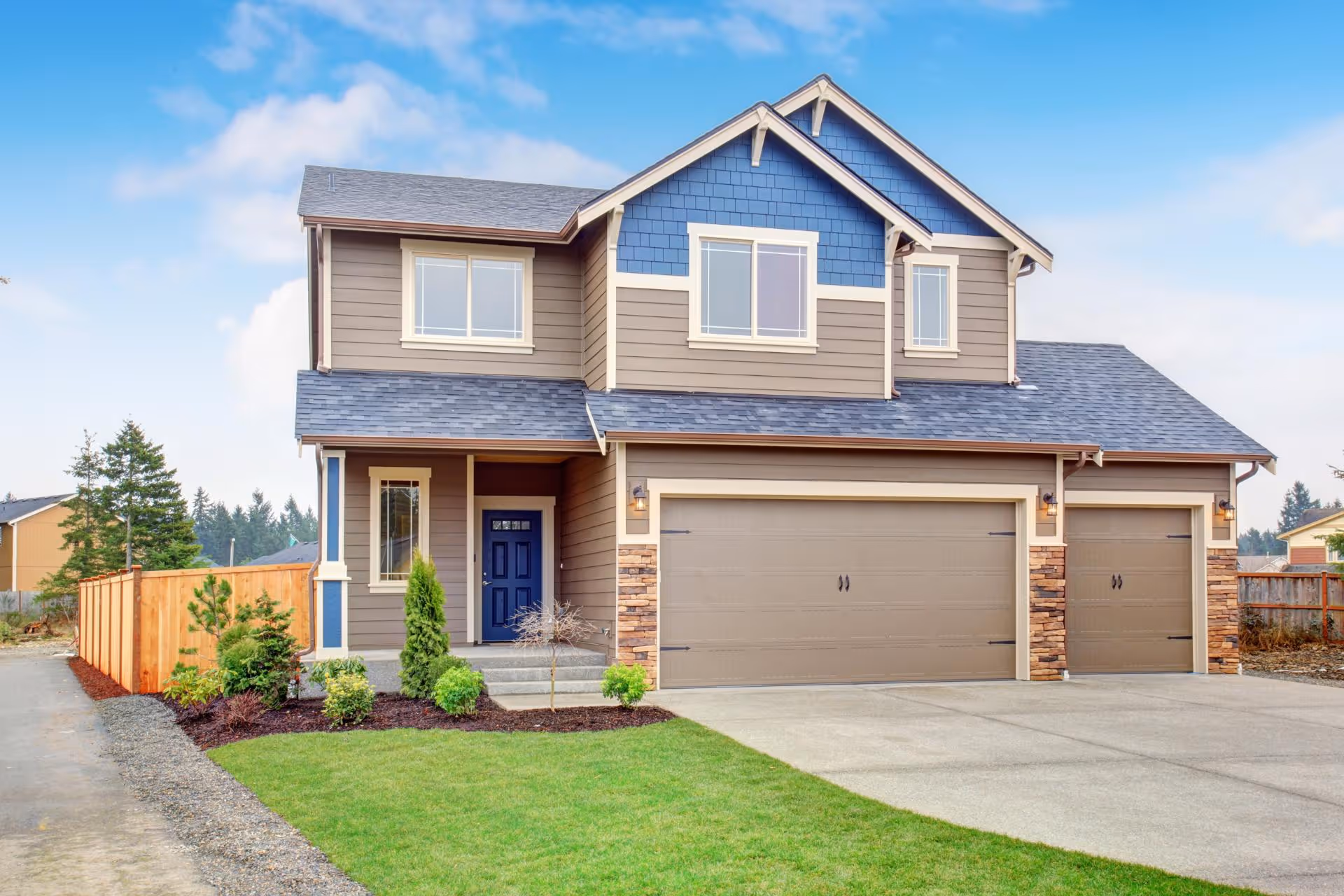 Two-story modern house with blue and brown siding, a three-car garage, and a neatly maintained lawn.