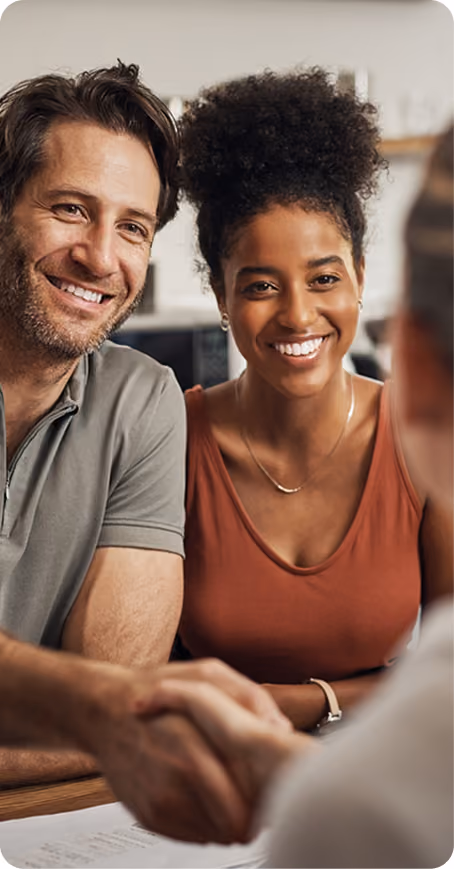 Smiling couple shaking hands with a person across a table in a modern setting.