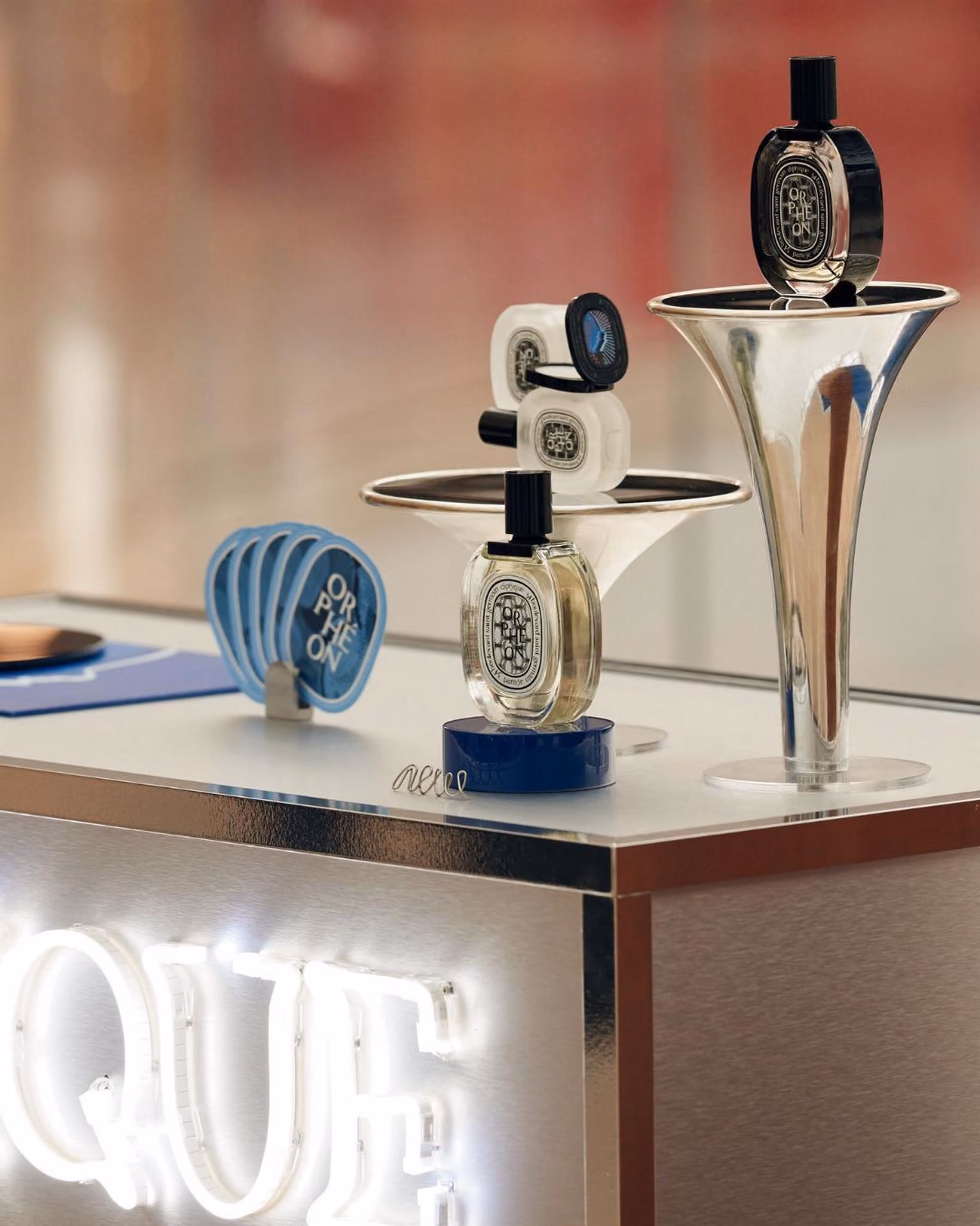 Display of Diptyque Orphéon perfume bottles and accessories on metallic surfaces.