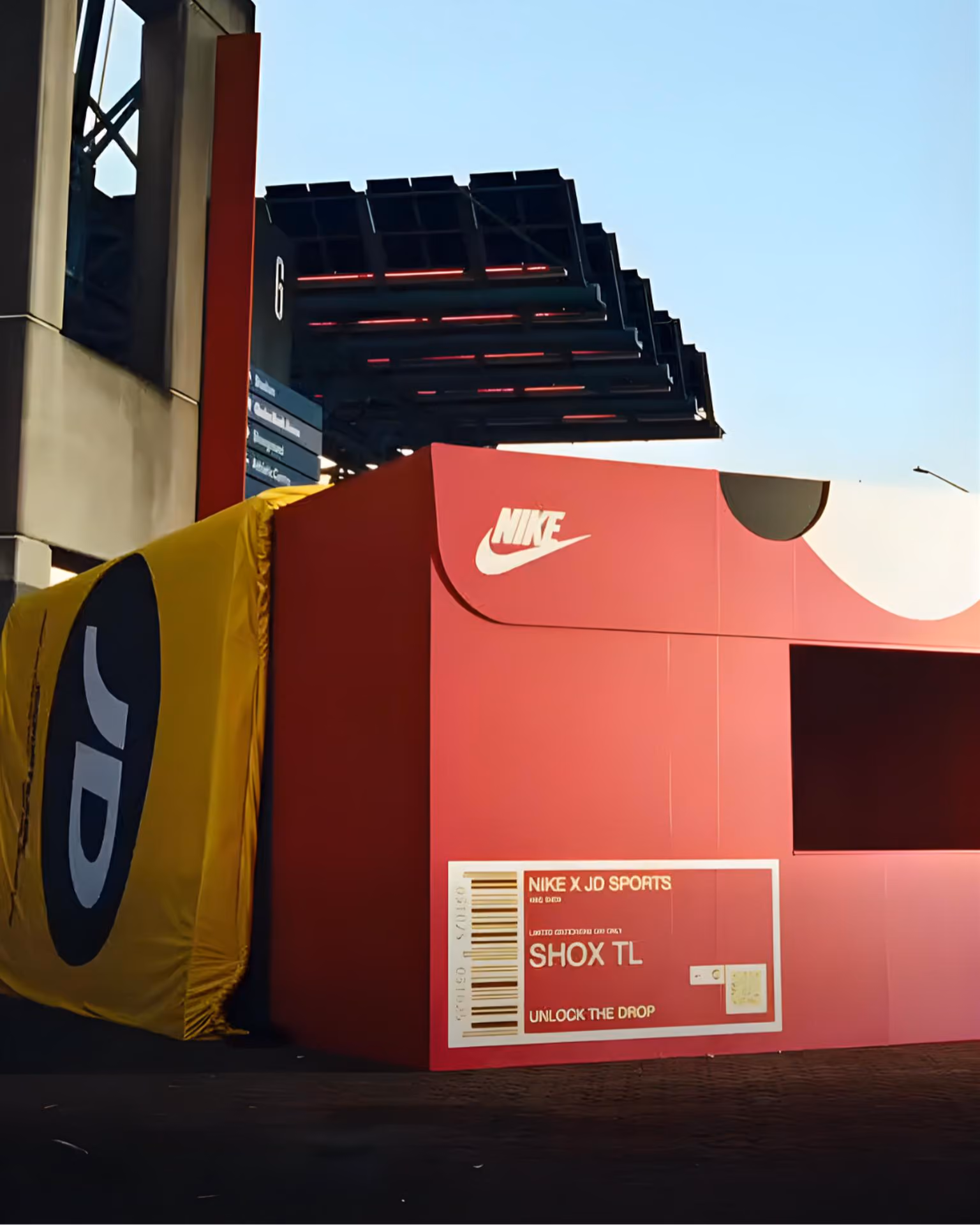 Large red Nike shoebox display with JD Sports branding outdoors under a clear sky.