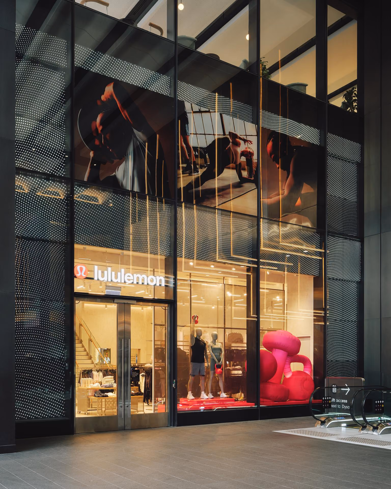 Lululemon store front with mannequins holding kettlebells and large pink kettlebell display in window.