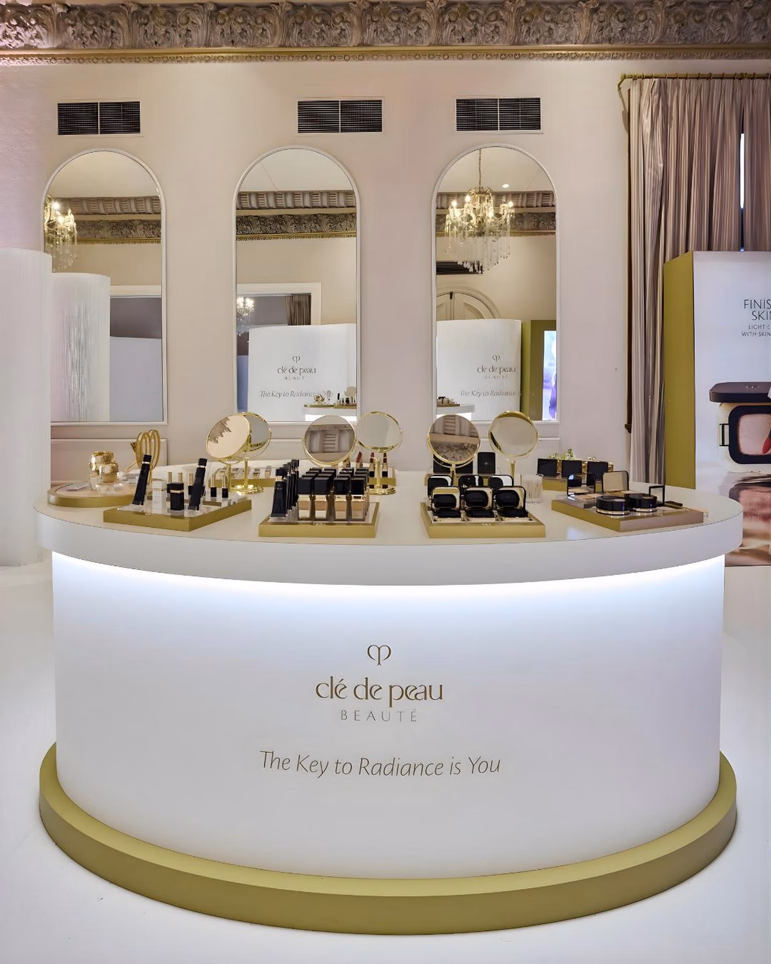Clé de Peau Beauté makeup display with mirrors and products on a round white illuminated counter.