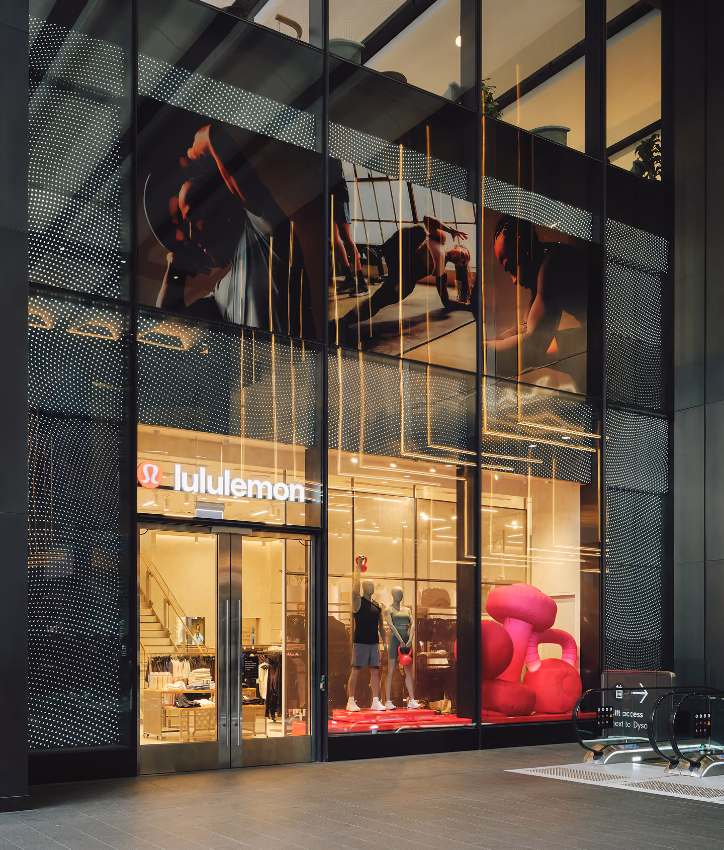 Lululemon store front with mannequins holding kettlebells and large pink inflatable shapes inside.