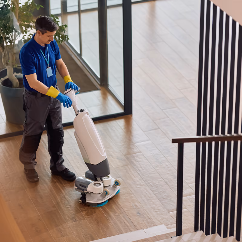 Reinigungskraft führt eine Bodenreinigungsmaschine durch einen Hausflur
