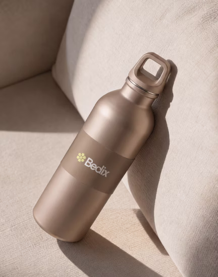 Matte bronze metal water bottle labeled 'Bedix' leaning on beige fabric surface.