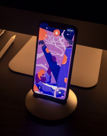 Smartphone with colorful abstract art wallpaper on a round stand in a dimly lit room.