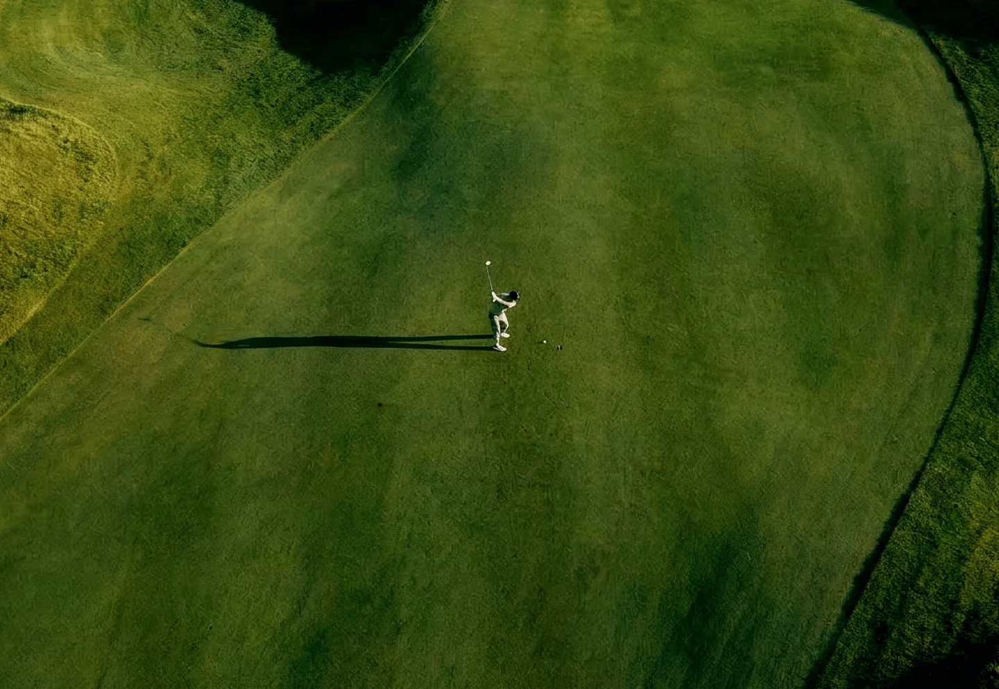 Aerial view of a golfer mid-swing on a green fairway