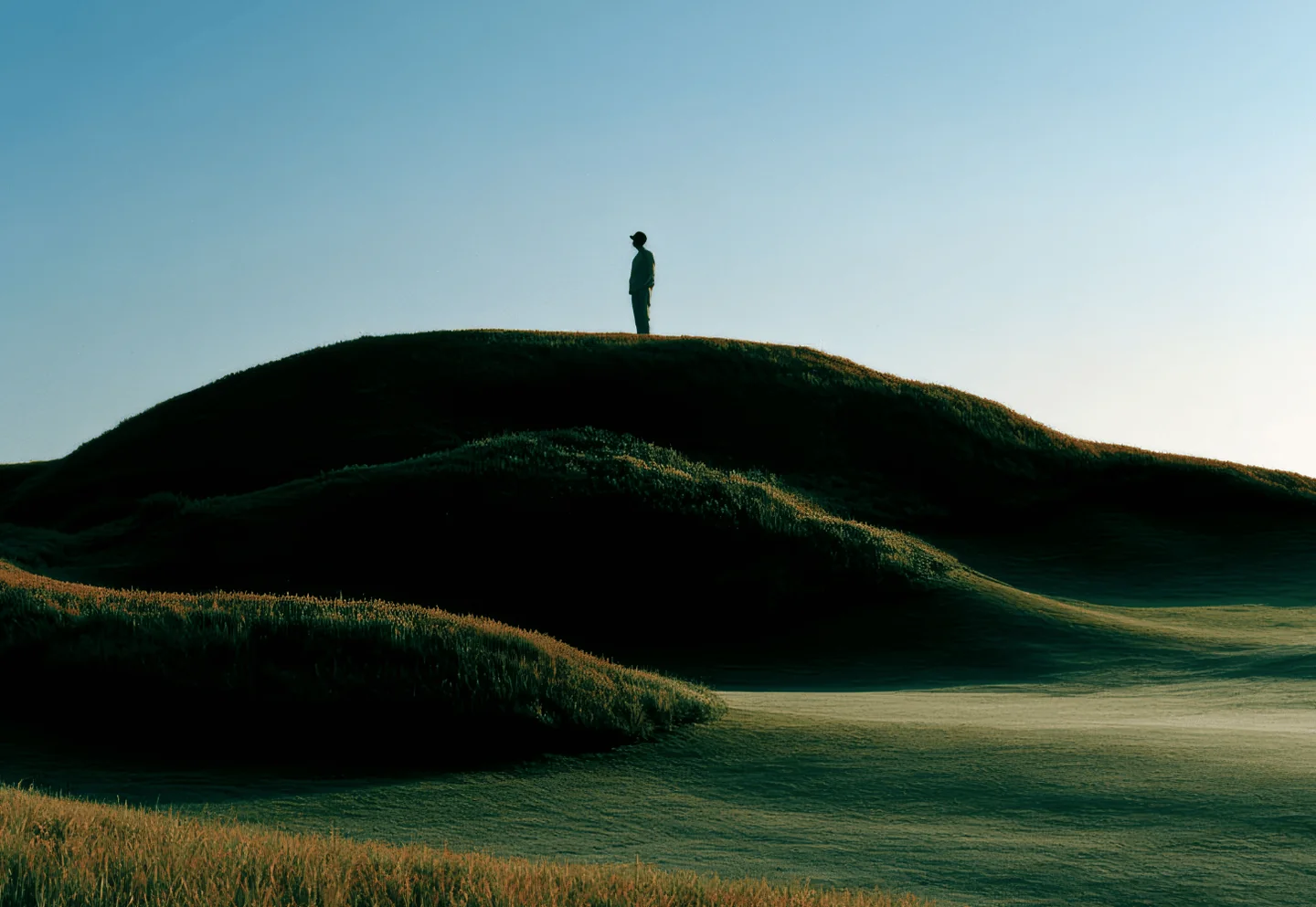 A lone figure on a green hill at dusk