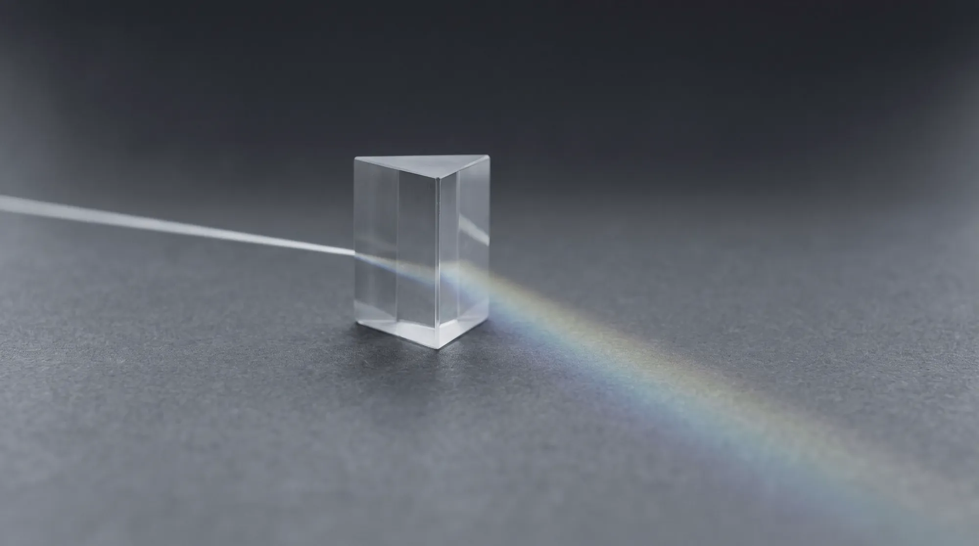 A glass prism splitting a single beam of light on a charcoal surface
