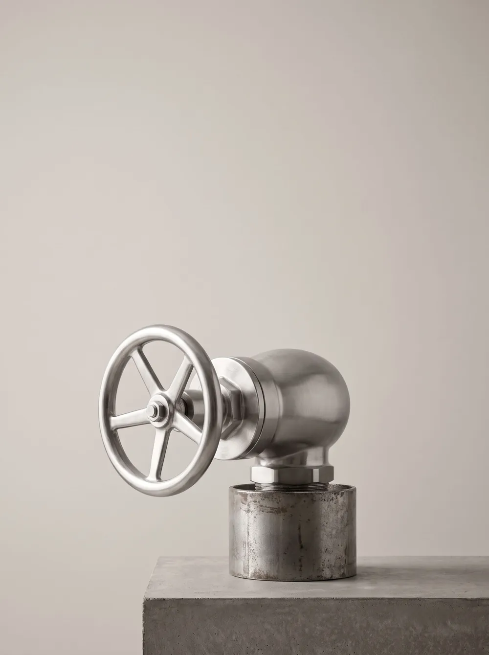 A chrome valve with a round handwheel against a pale wall