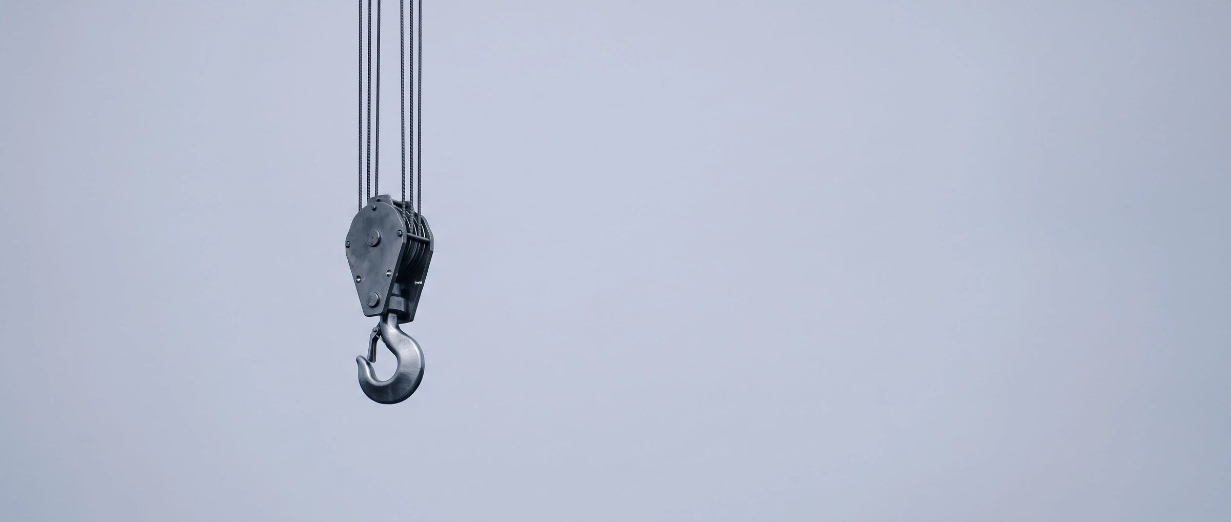 Steel crane hook hanging against a pale overcast sky
