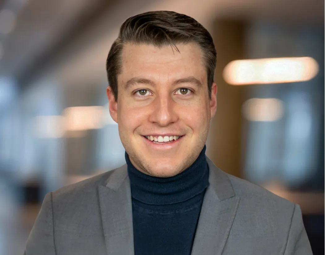 Homme souriant portant un col roulé bleu foncé et un blazer gris dans un bureau flou