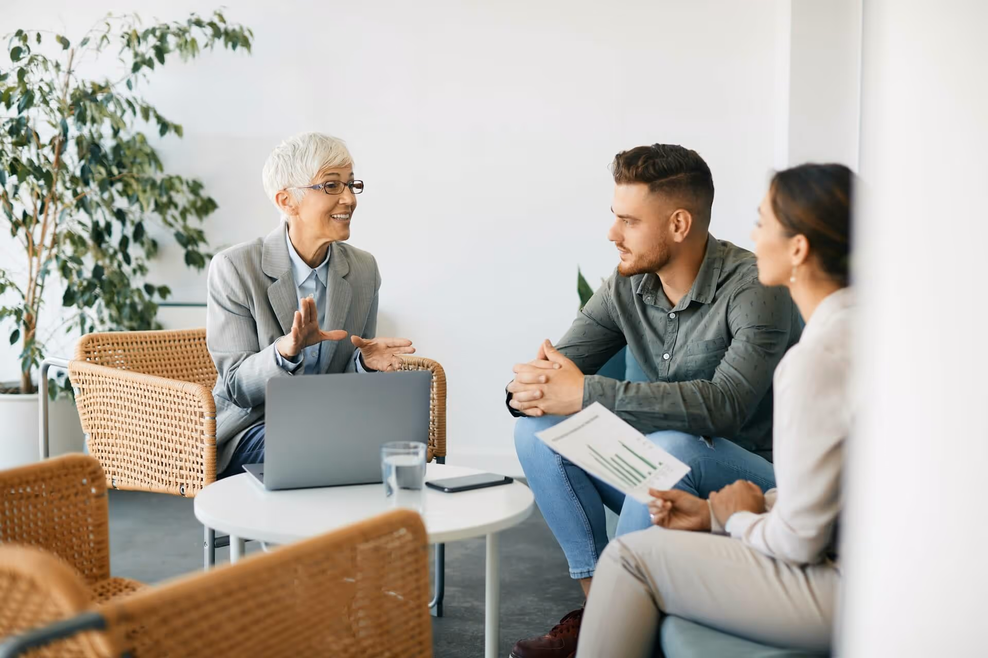 Businesswoman discussing financial charts with young couple in modern office setting.