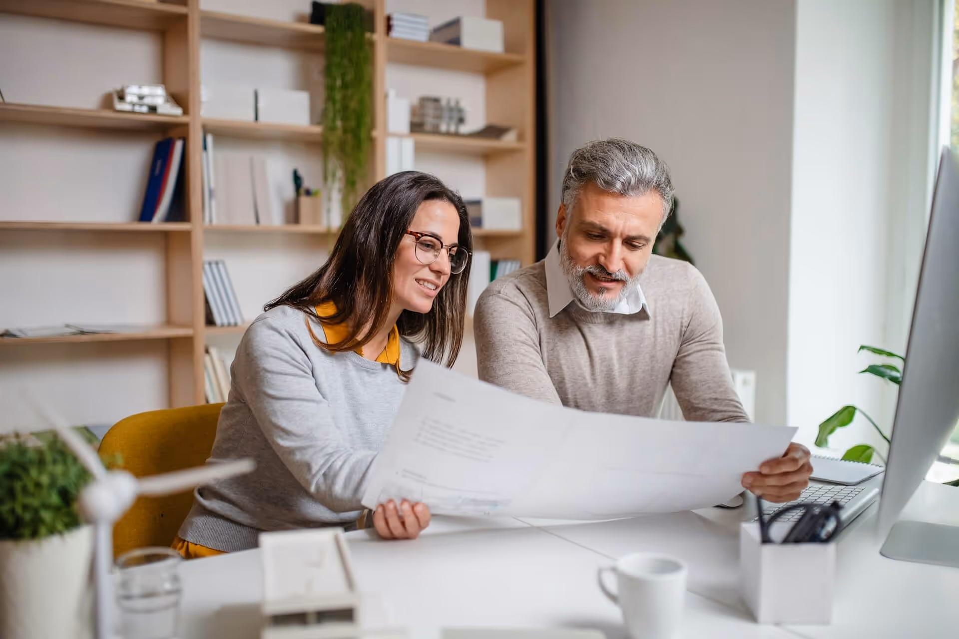 Man and woman reviewing large paper plans together at a desk in a modern office.