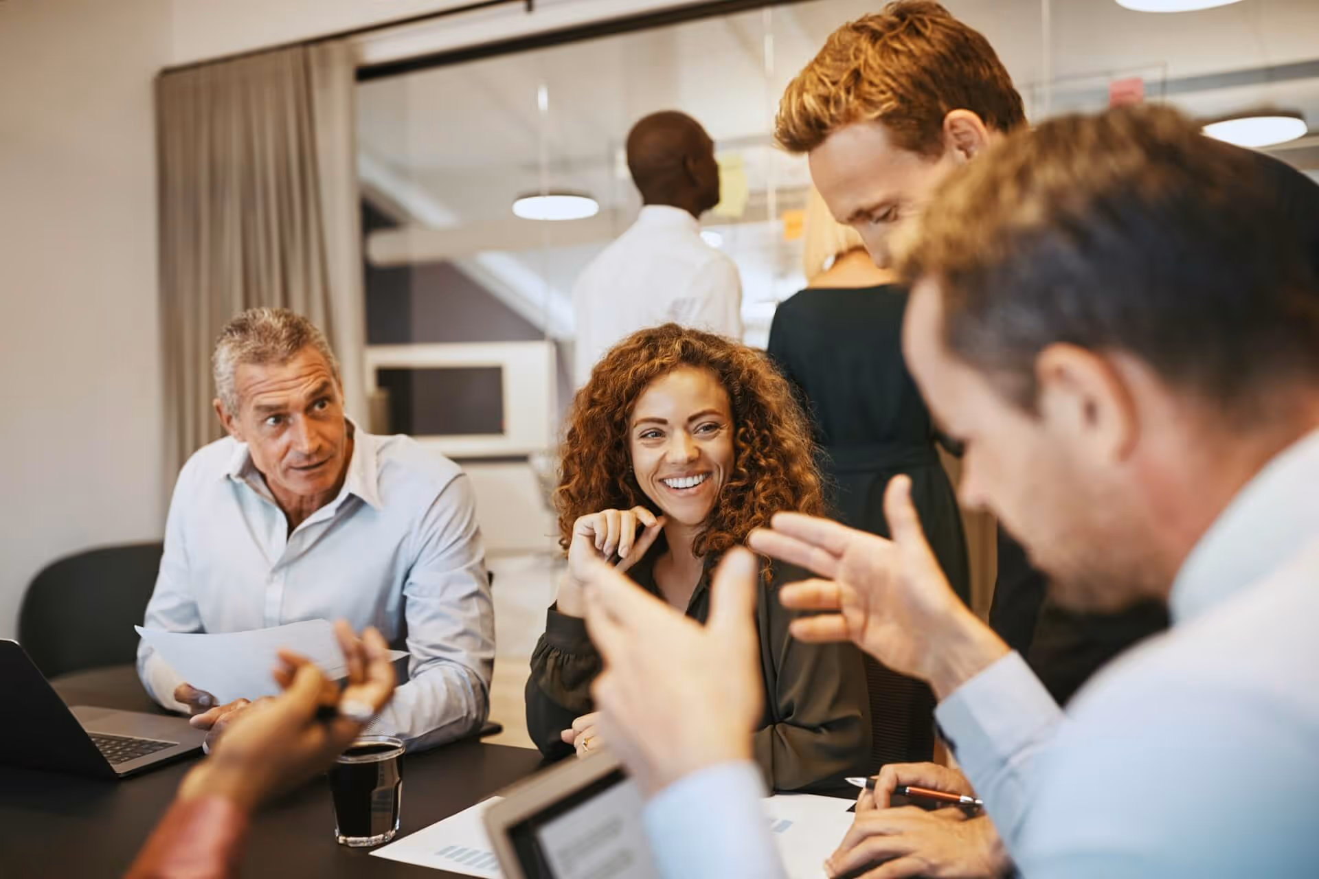 Diverse group of colleagues discussing and smiling in a modern office meeting.