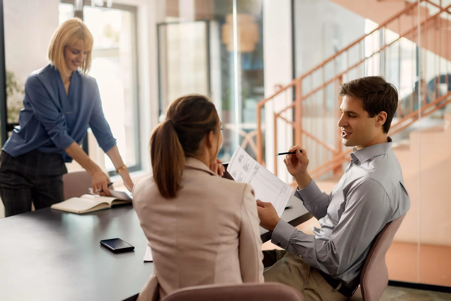 Three coworkers discussing documents together around a table in a modern office space.