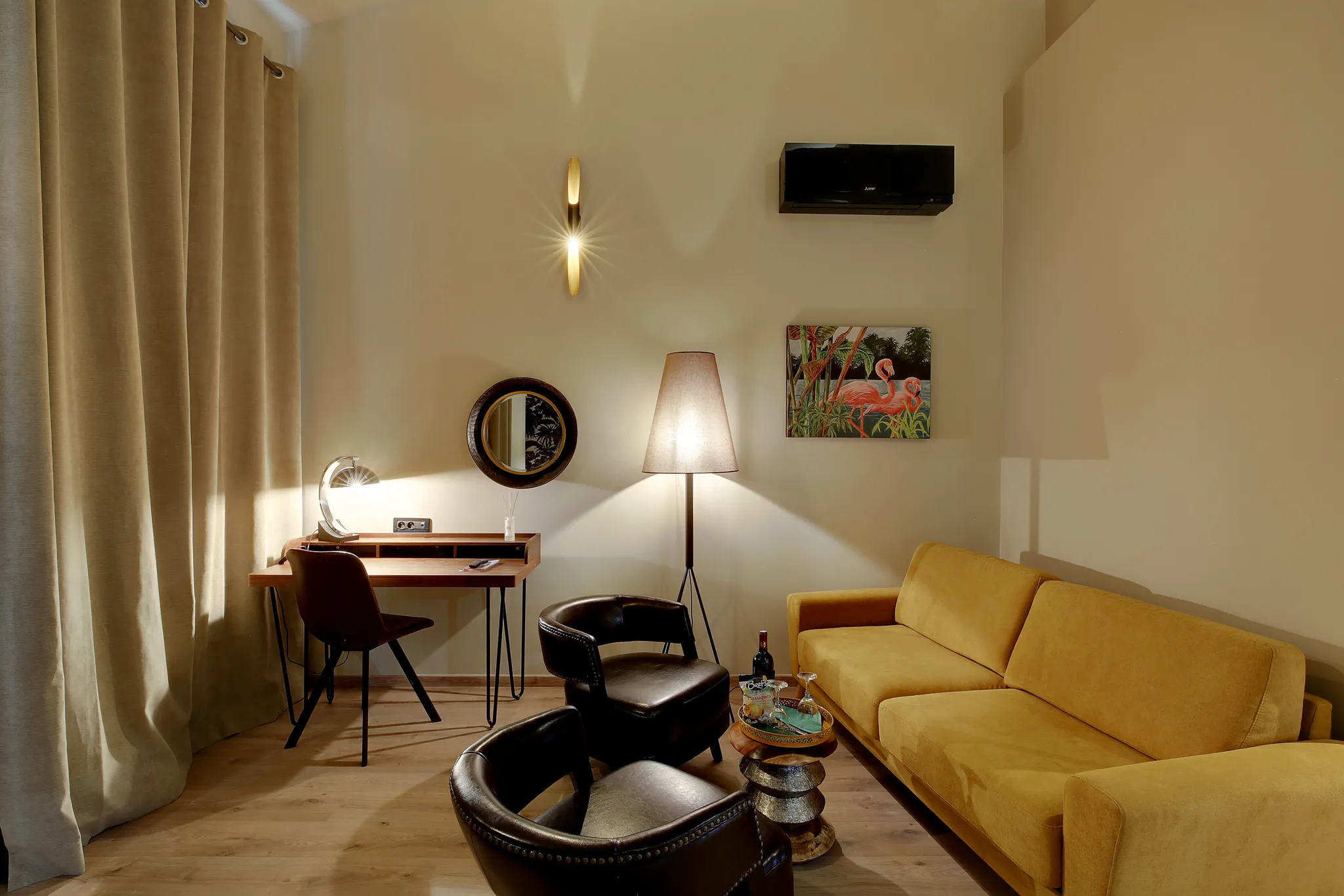 Salon avec canapé jaune, deux fauteuils noirs, bureau, lampadaire et tableau de flamants roses.