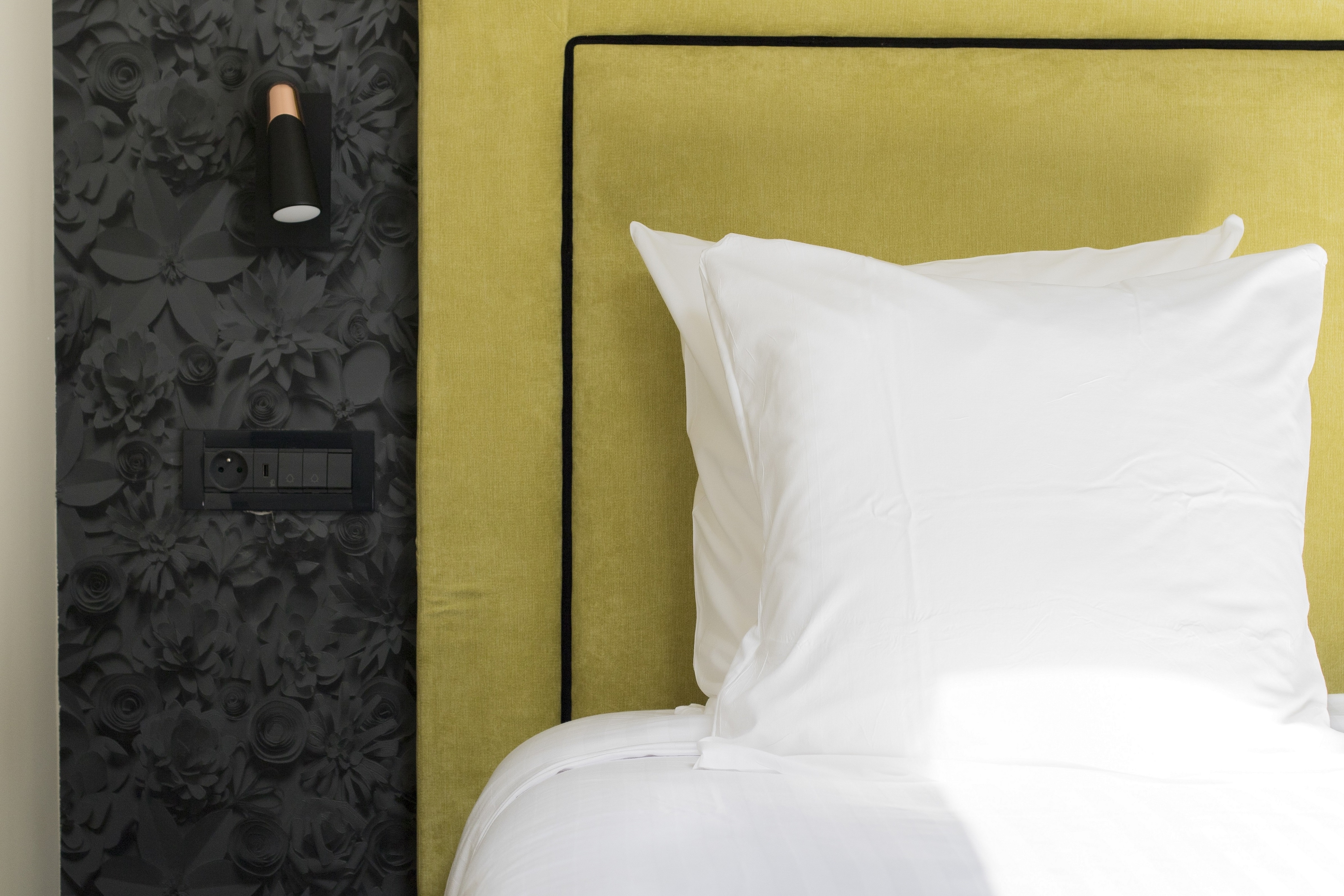 Coussin blanc sur un lit avec une tête de lit jaune et un mur noir à motifs floraux.