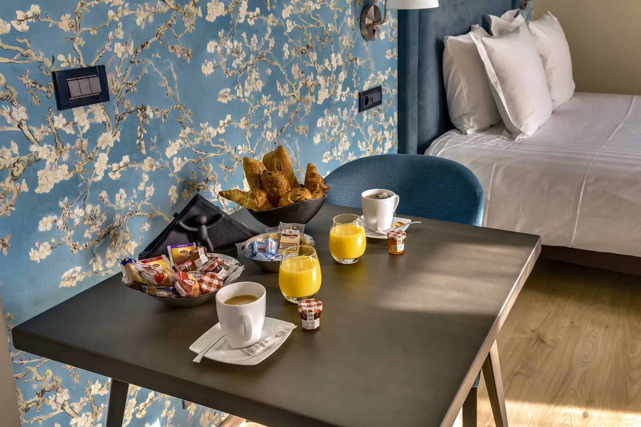 Table avec petit déjeuner: café, jus d'orange, croissants, confitures dans une chambre décorée.