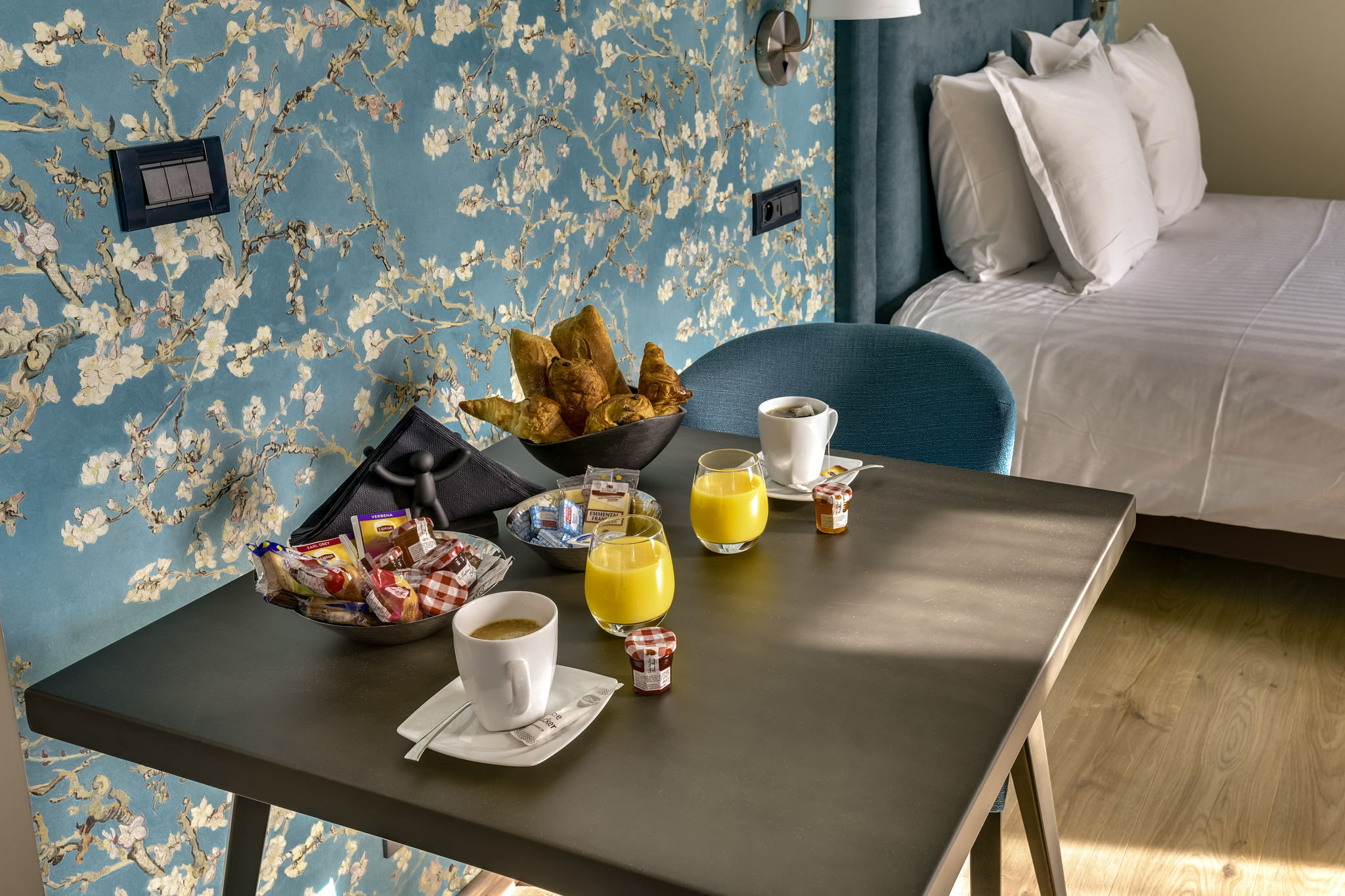 Table avec petit déjeuner: café, jus d'orange, croissants, confitures dans une chambre décorée.
