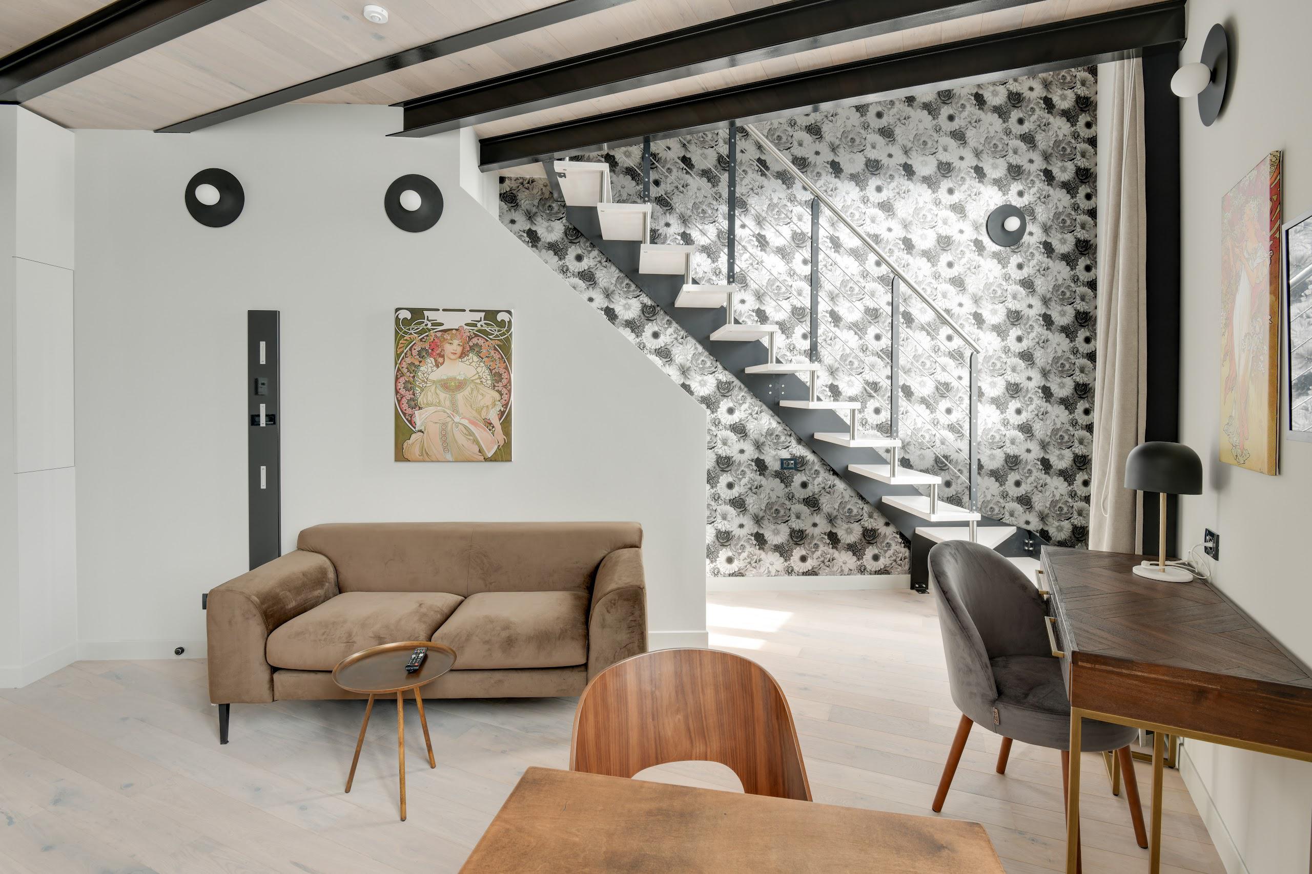 Salon moderne avec un canapé brun, une table ronde, un escalier à motif floral noir et blanc.