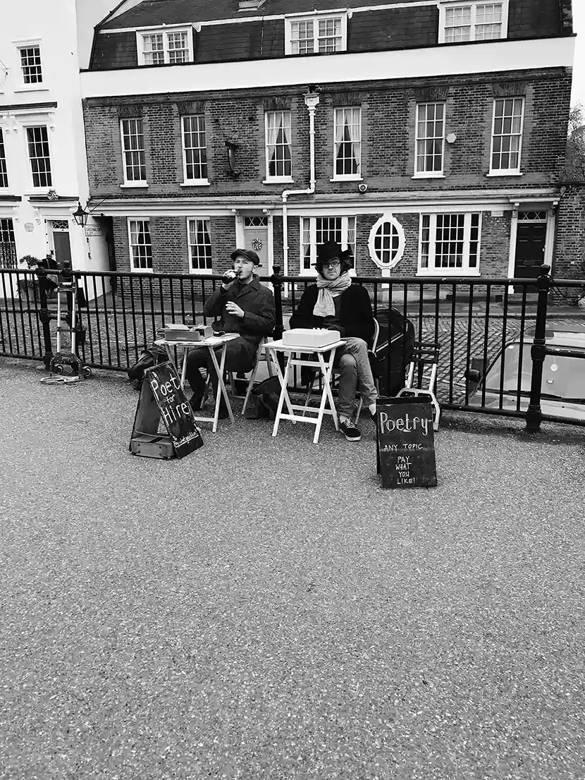 Black-and-white street photo of two men at a poetry stall, captured by Ampersand team member Jill Wang