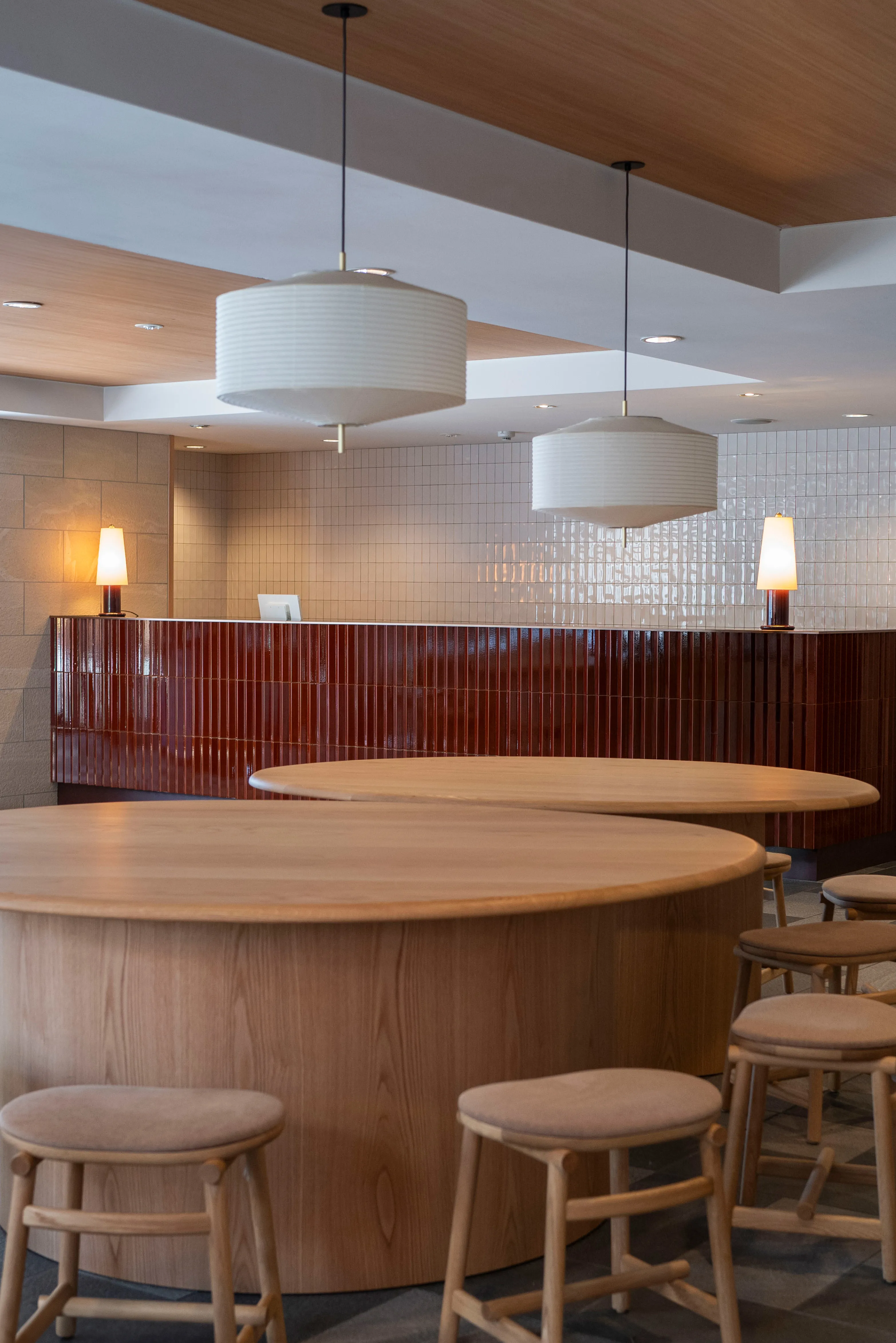 Glad One hotel lobby in Kyoto, minimalist Japanese style, brick-red counter, white lantern light, round wood tables