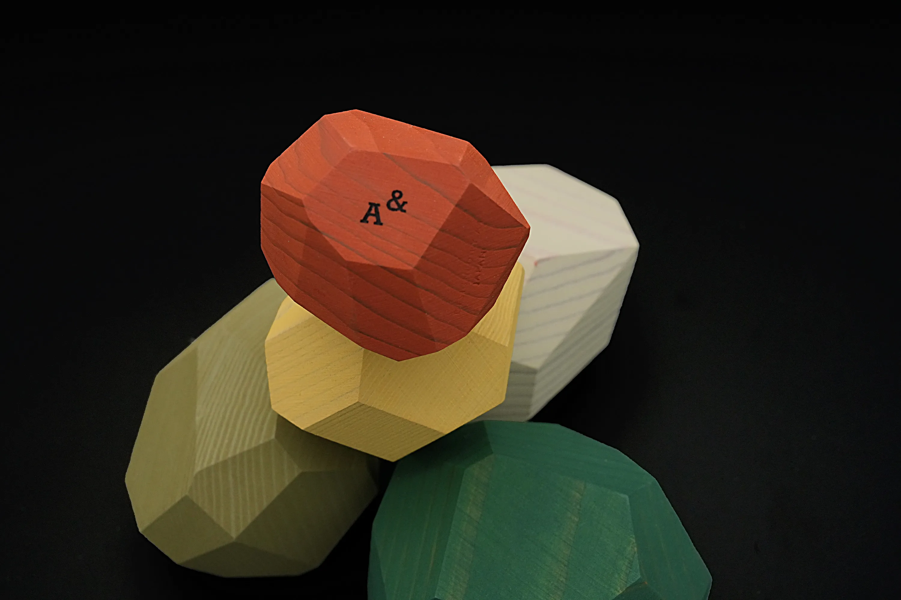 Close-up of an orange faceted wooden block with "A&" mark, part of Ampersand's tumi-isi stacking set