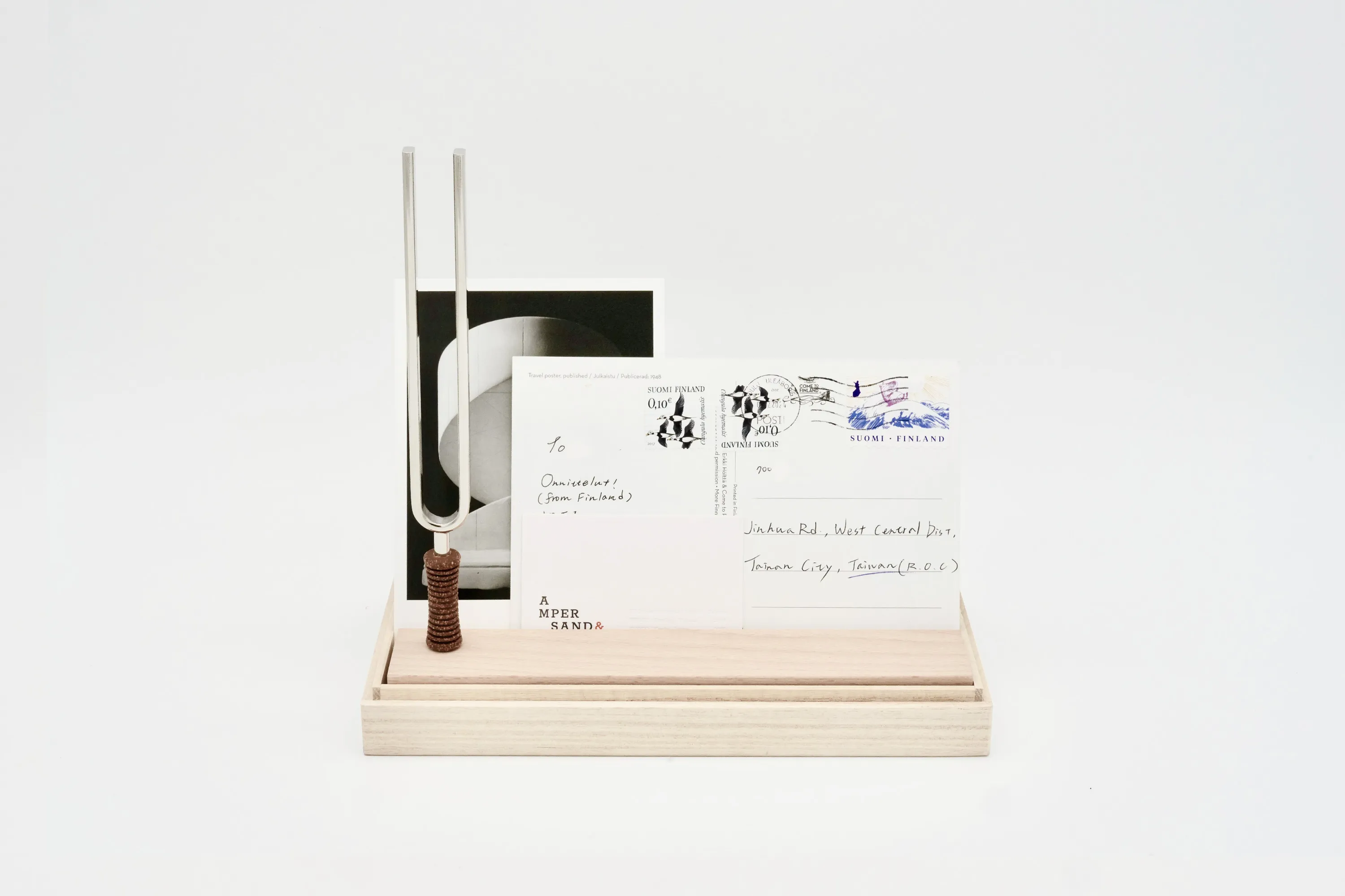 Tuning fork on wooden stand beside a handwritten postcard and Ampersand business card
