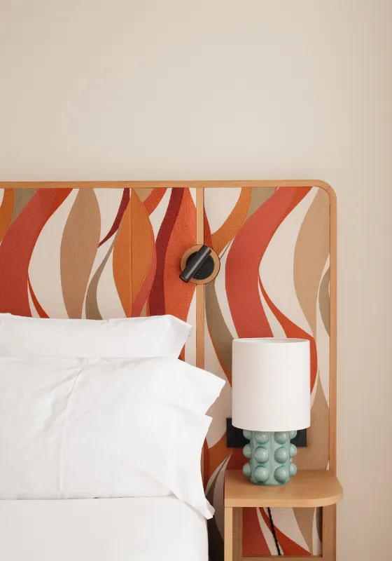 Tête de lit avec motif orange et beige, lampe verte sur table de chevet à côté d'un lit avec oreillers blancs.