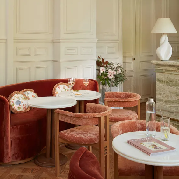 Coin salon élégant avec fauteuils velours rouille, tables rondes blanches, plantes et décor lumineux.