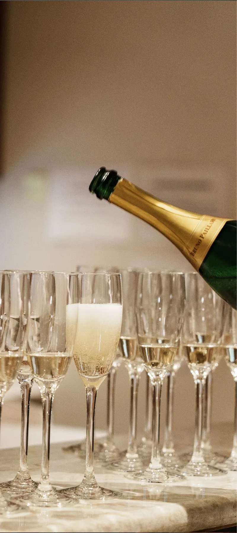Bouteille de champagne versant du champagne dans une rangée de flûtes sur une table.