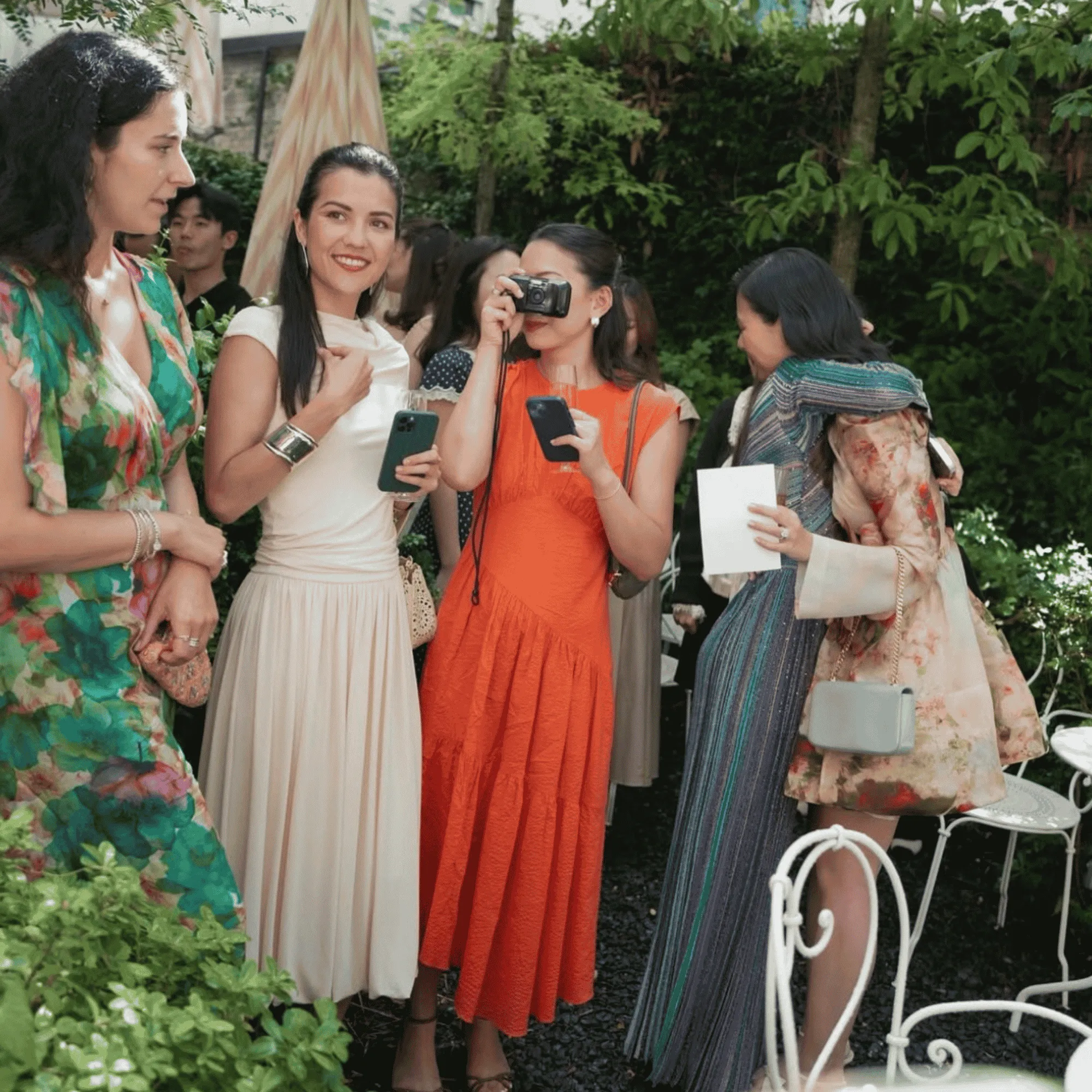 Groupe de femmes élégantes en robe discutant dans un jardin lors d'un événement social.