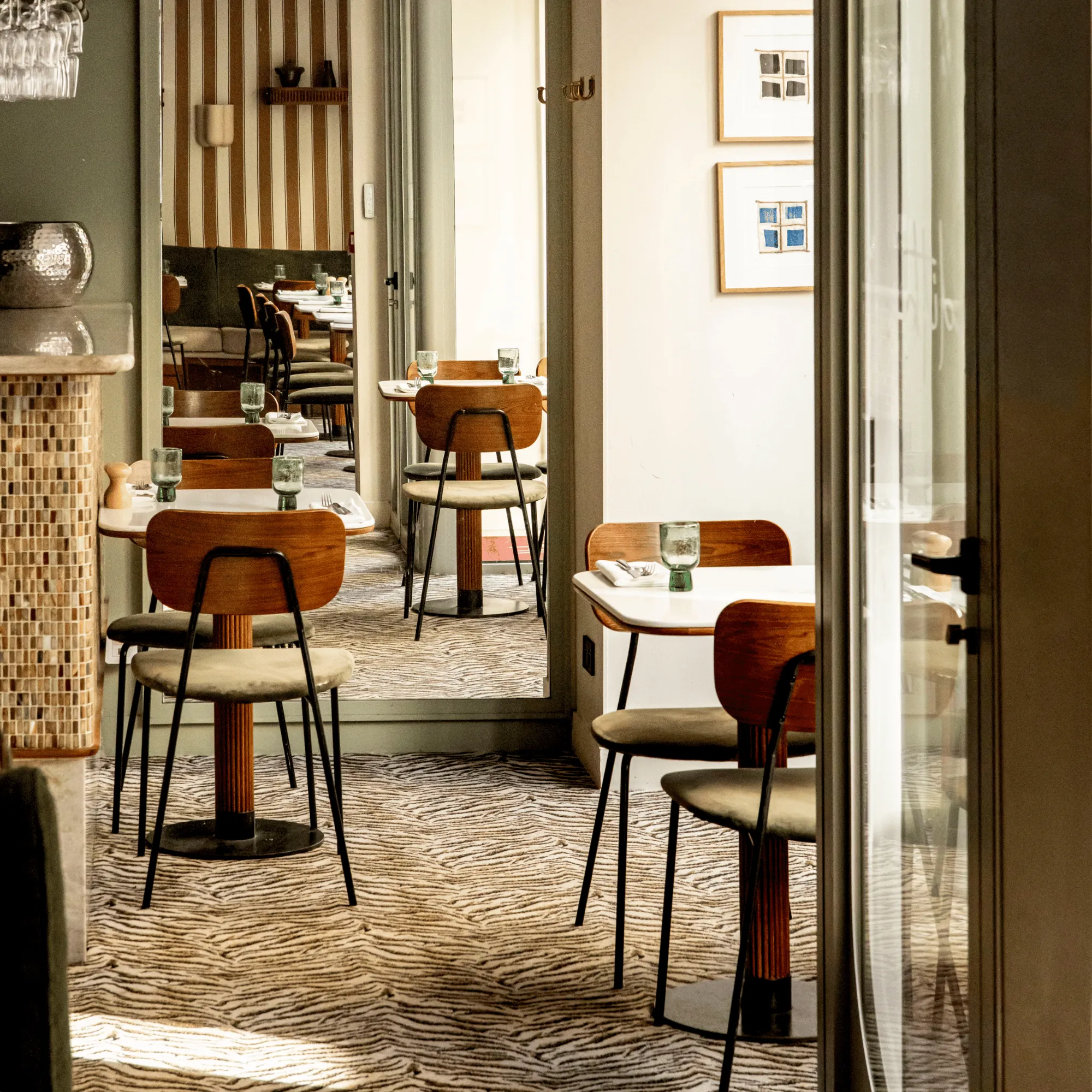 Intérieur d'un café avec petites tables blanches, chaises en bois et sol à motif animalier.