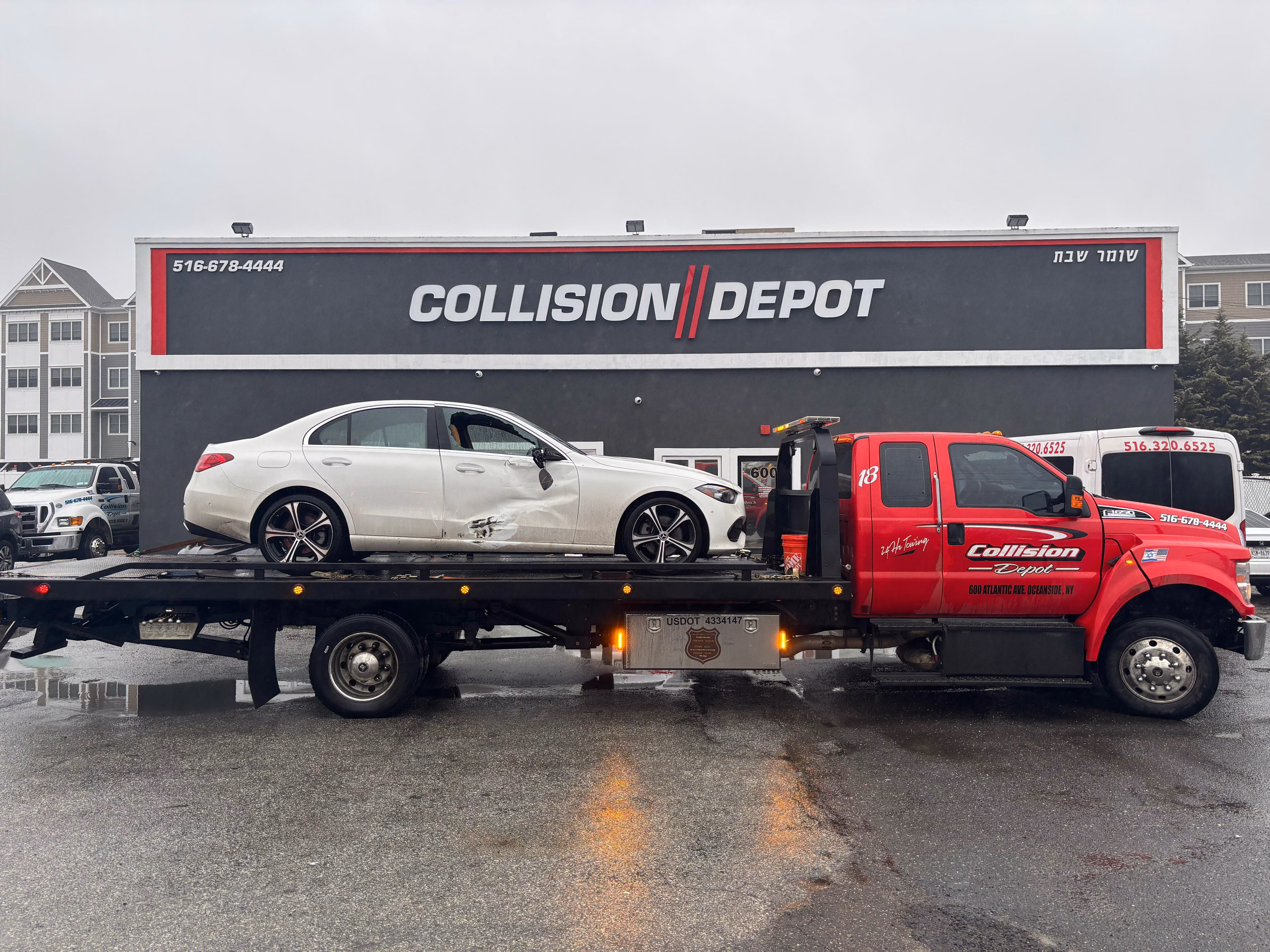A red Collision Depot tow truck with a damaged white sedan on its flatbed in front of a gray Collision Depot building with large white and red signage and a contact phone number.