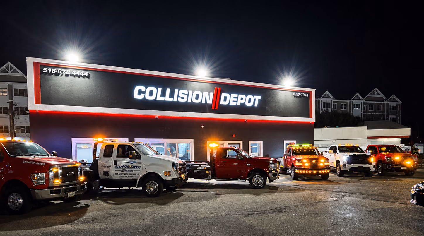 Nighttime view of Collision Depot building with illuminated sign and six tow trucks with flashing lights parked in front.