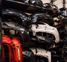 Stacked car bumpers in various colors including black, white, and red, arranged on a storage rack in a warehouse.