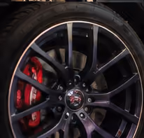 Close-up of a black car wheel with a multi-spoke alloy rim and a red brake caliper visible behind the spokes.